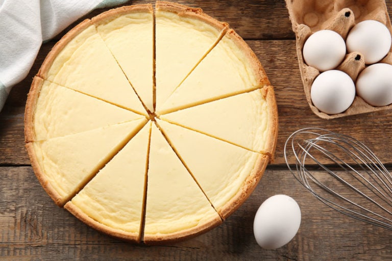 Tasty homemade cheesecake, eggs and whisk on wooden table